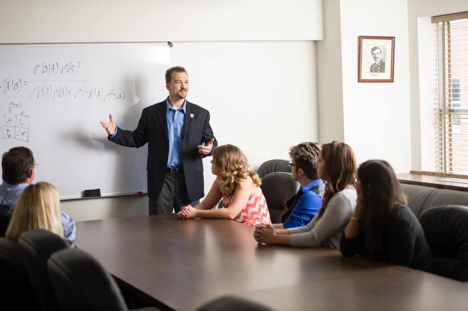 Psychology instructor teaching class around a large boardroom table.