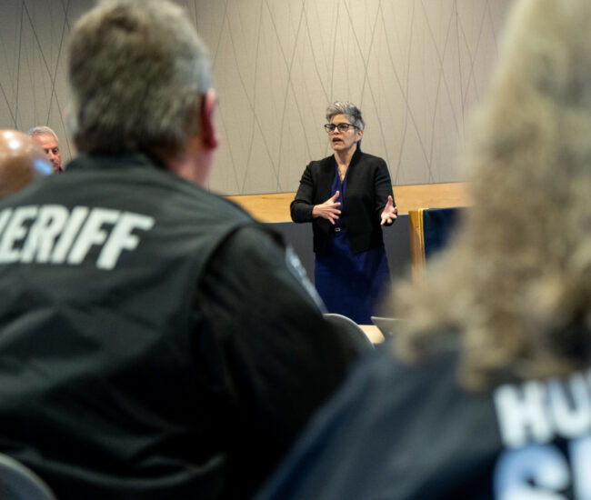 Faculty member instructing class with two class mates wearing sheriff uniform jackets.