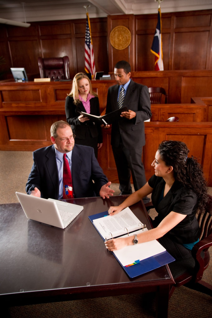 Man and Woman at table in courtroom with another man and woman discussing a case in the background