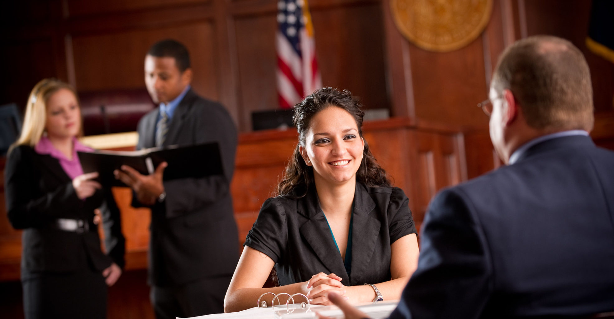 Woman approaching judges desk with individual discussing a case in the background.