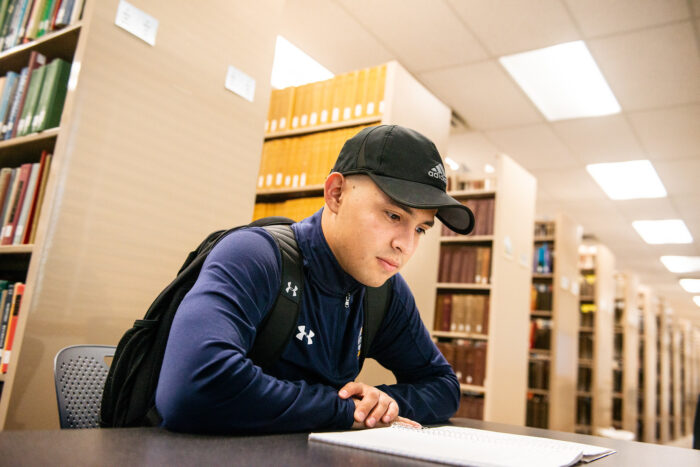 Male student reading a book in a library.