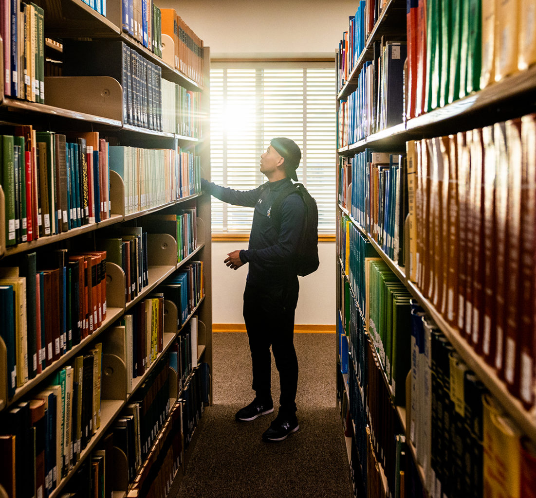 Male student looking for a book in the library.