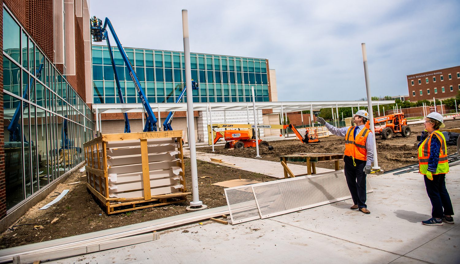 Construction workers discussing the project they are working on. While other workers are working in the background.