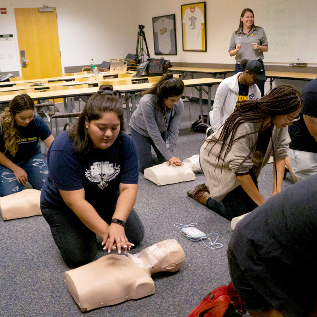 Students on the floor in front of a mannequin during a CPR class.
