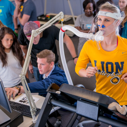 Professor and students observing a health and human performance test including a female athlete running on treadmill.