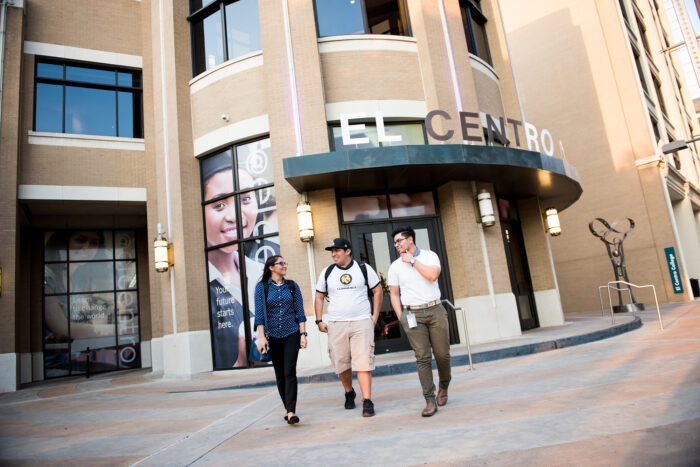 Multiple students walking out of the ElCentro College. One female dressed in blue. The other two men are dressed in white.