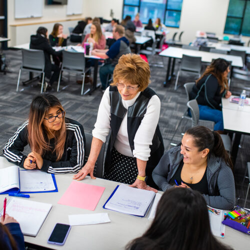 A professor having a conversation with a group of student sitting down in class.