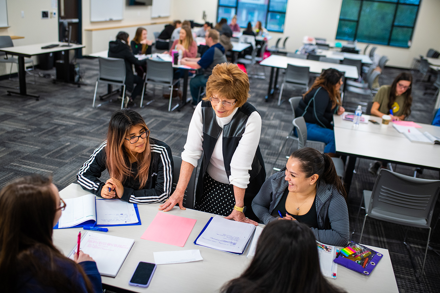 A female professor talking to a group of student sitting down in class.