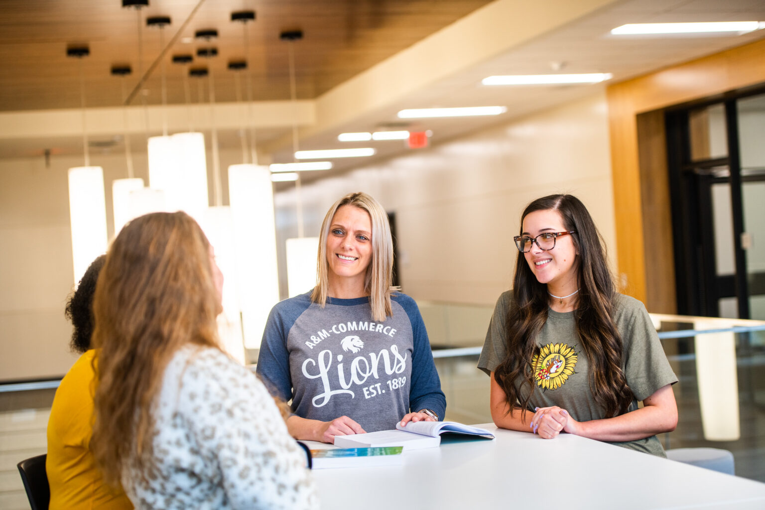 A group of 4 females talking with a book open on a table.