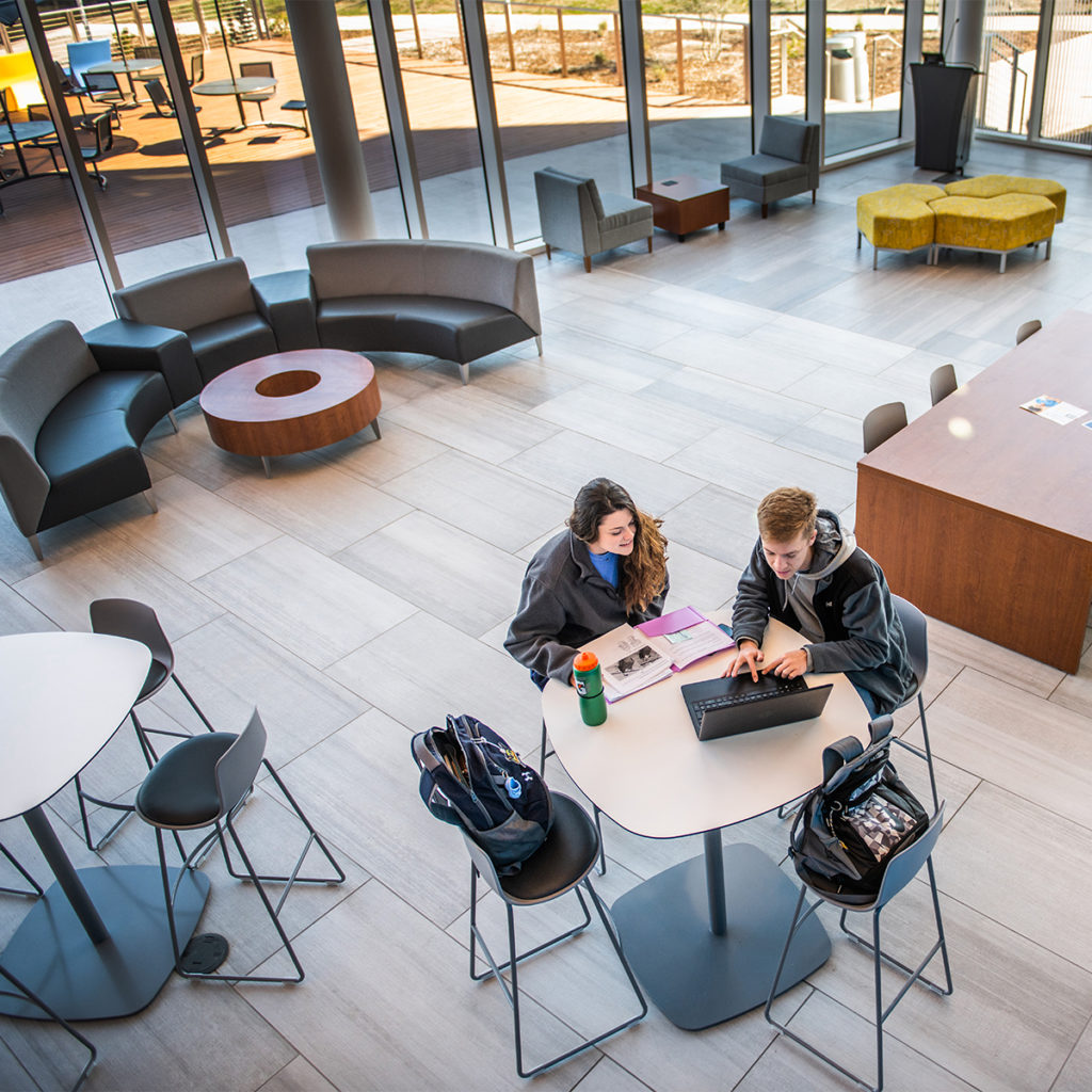 Two student sitting down at a table looking at a laptop in the common area of the nursing and health sciences building.