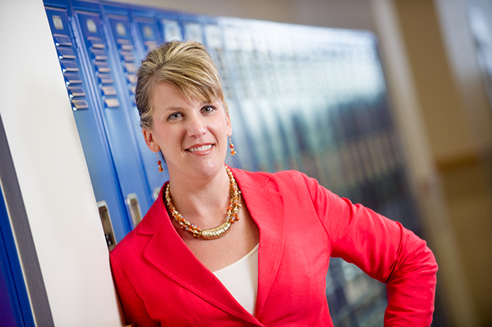 Woman teacher standing by lockers in the hallway.