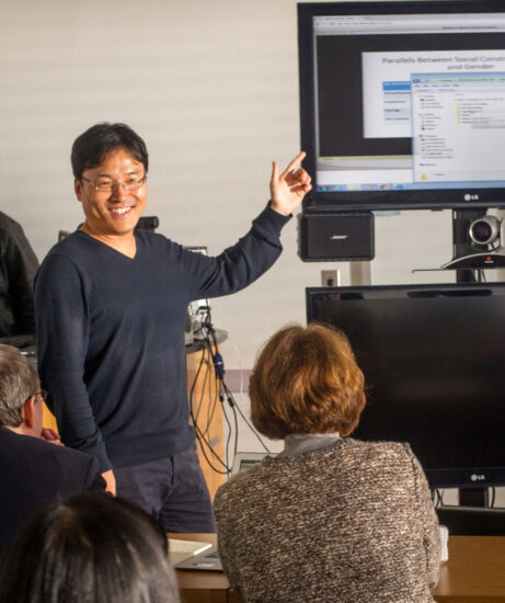 Man pointing to large computer screen while teaching class.
