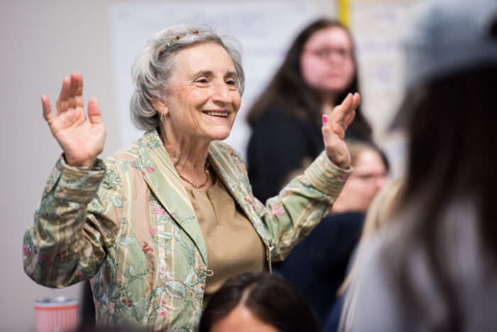 Older female educator standing in classroom with raised hands and smiling