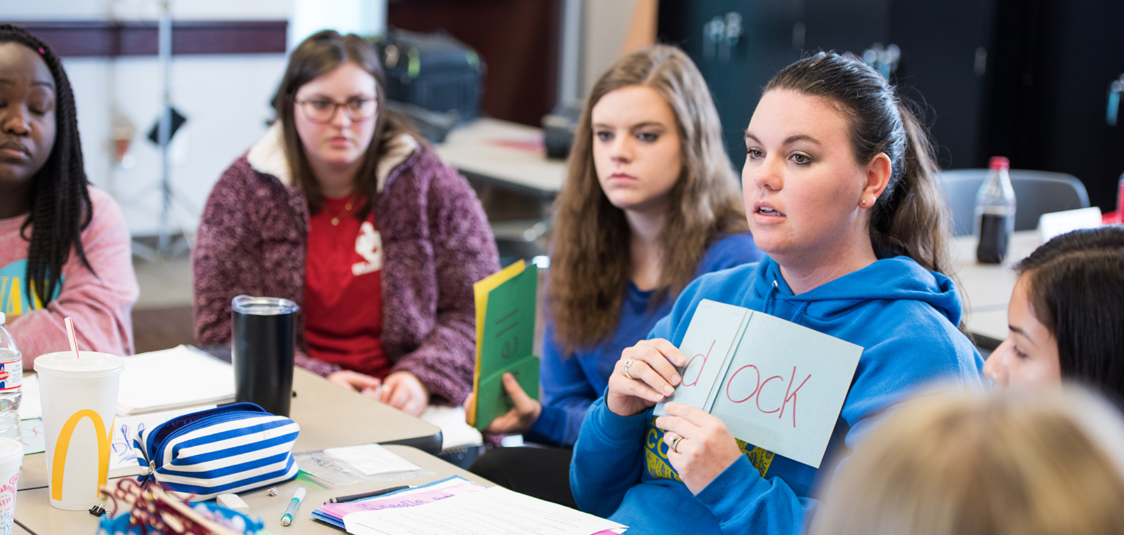 A student holding a blue piece of paper with a word wrote on it, in class.