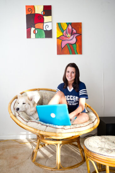 Female student on chair with dog and laptop working on online course.