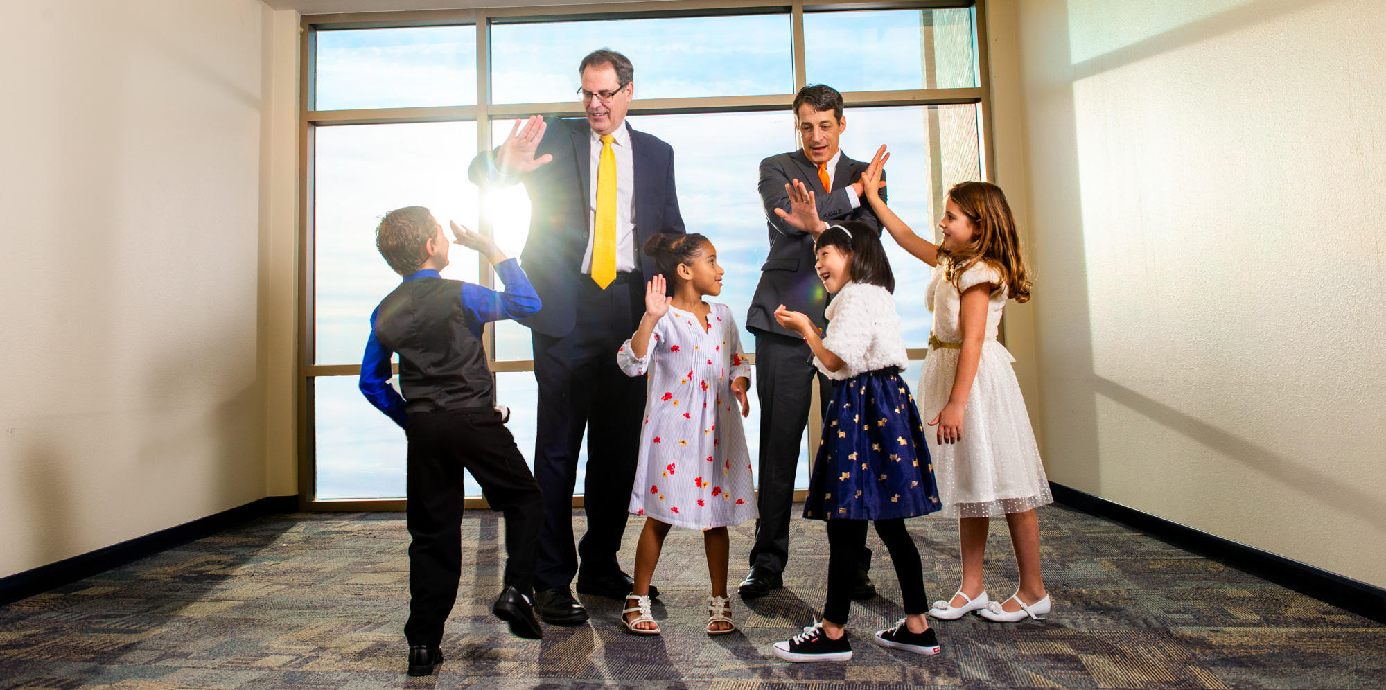 Two professionally dressed men giving high-fives to 4 young kids.