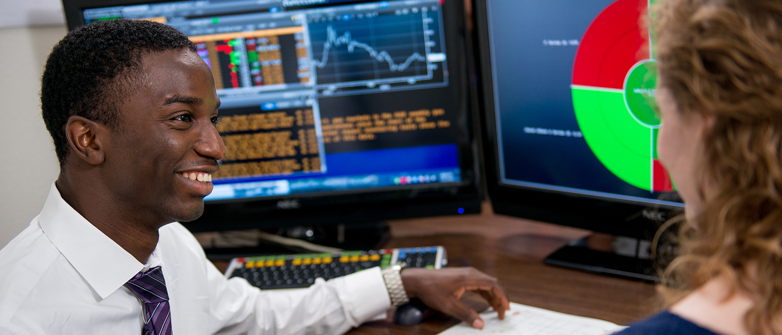 Analyst talking to another professional, with computer screens in the background.