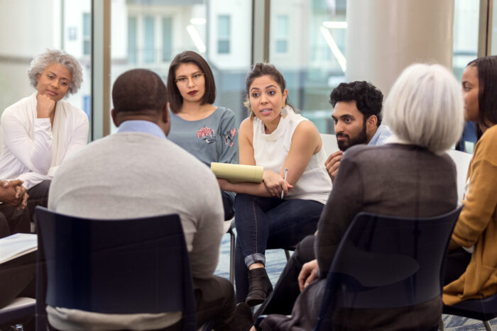 A group of people sitting down in a circle listening to a therapist.