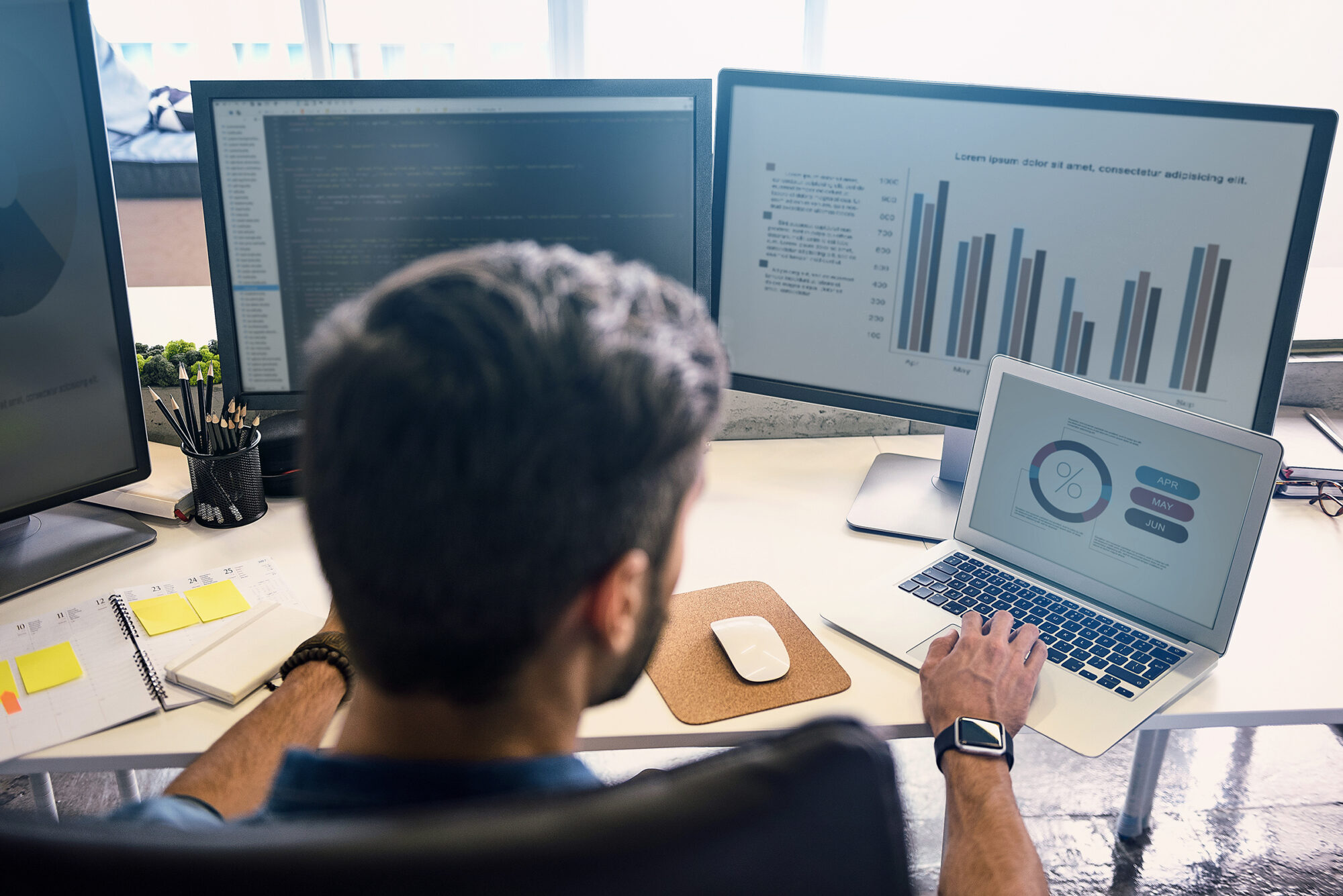 Analyst working in front of multiple computer screen.