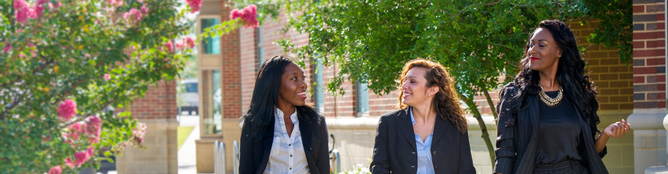 Three women walking together wearing professional attire.