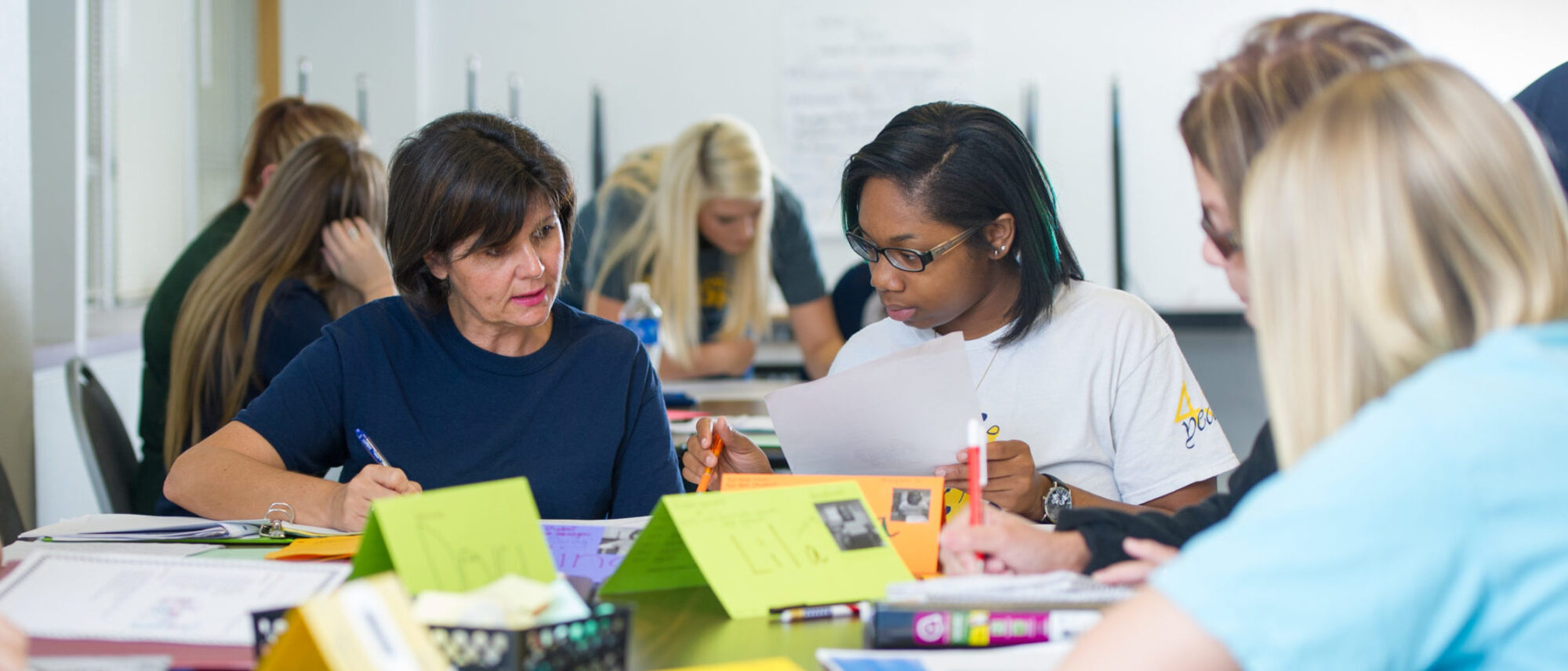 Two students working together while reading material on a desk.