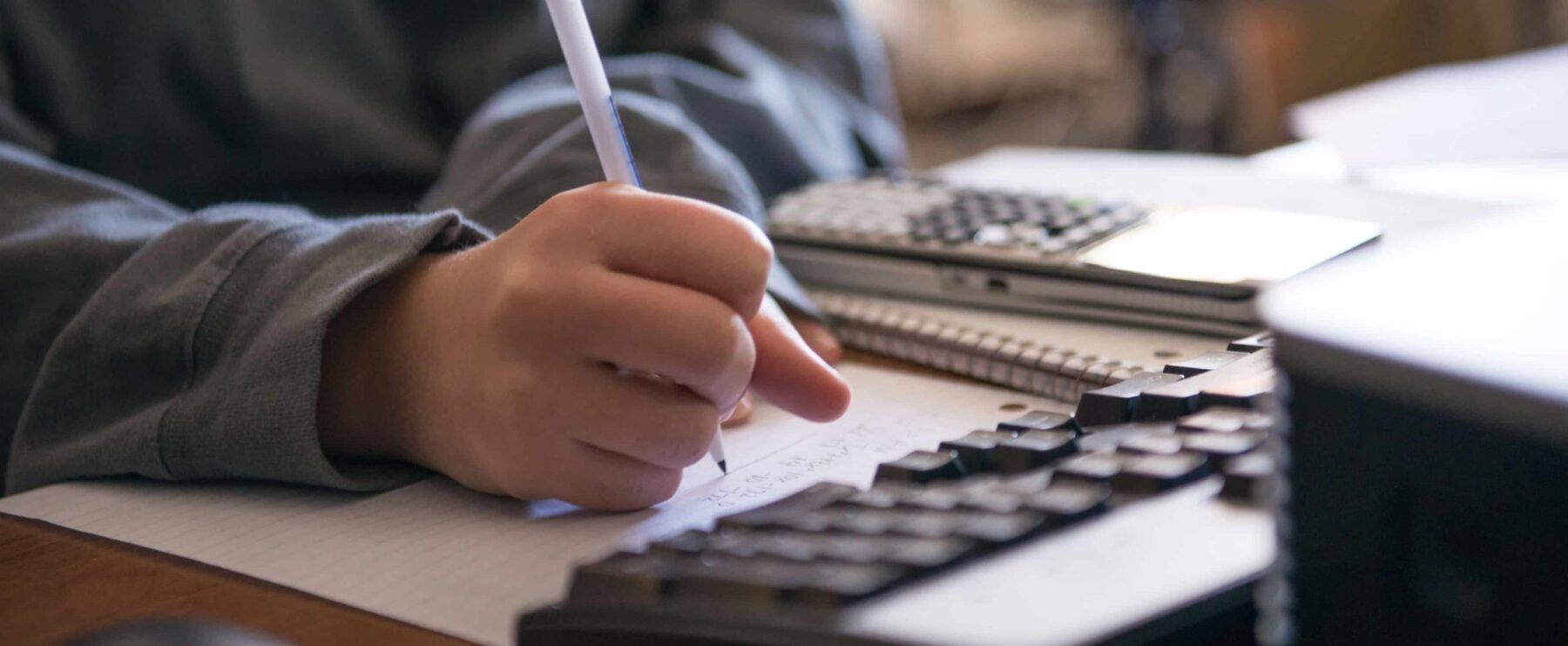 An individual completing a problem on paper in front of a computer.