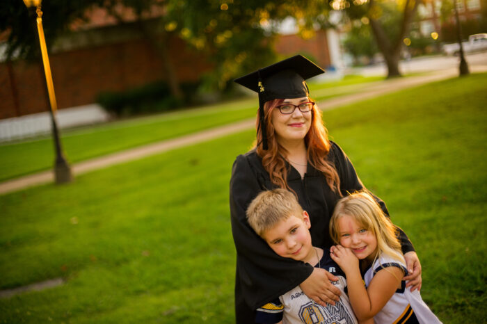 Graduate in cap and gown taking a picture with her kids.