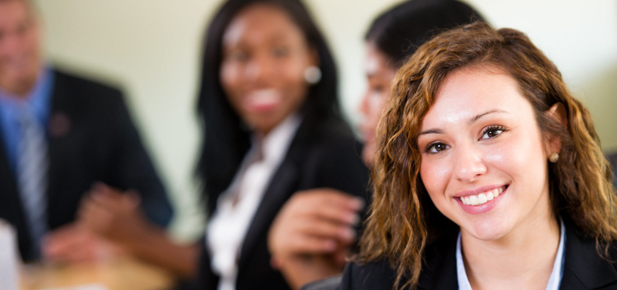 Young lady smiling with other professionally dressed students in the background.