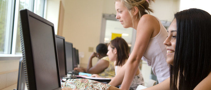A female student looking at the computer along with other students at different computers.