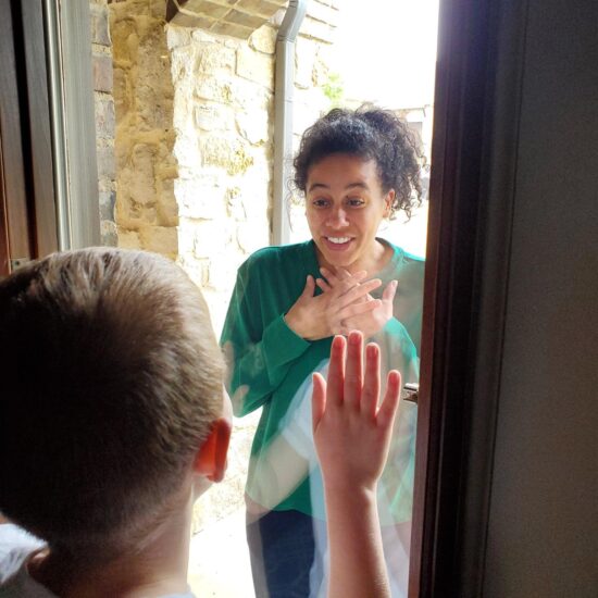 A teacher interacting with a student through the glass of their front door during pandamic.