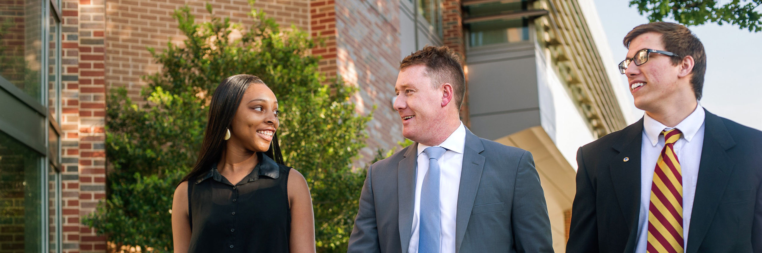 A group of people standing in front of a building smiling at each other and wearing business attire.