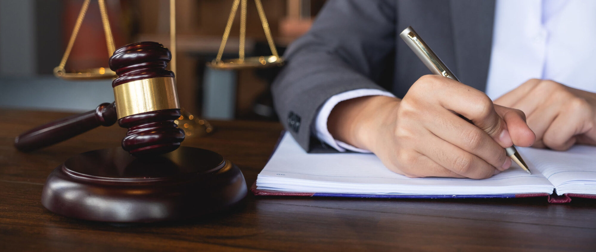 A person taking notes sitting at a table with a judge hammer beside the notebook.