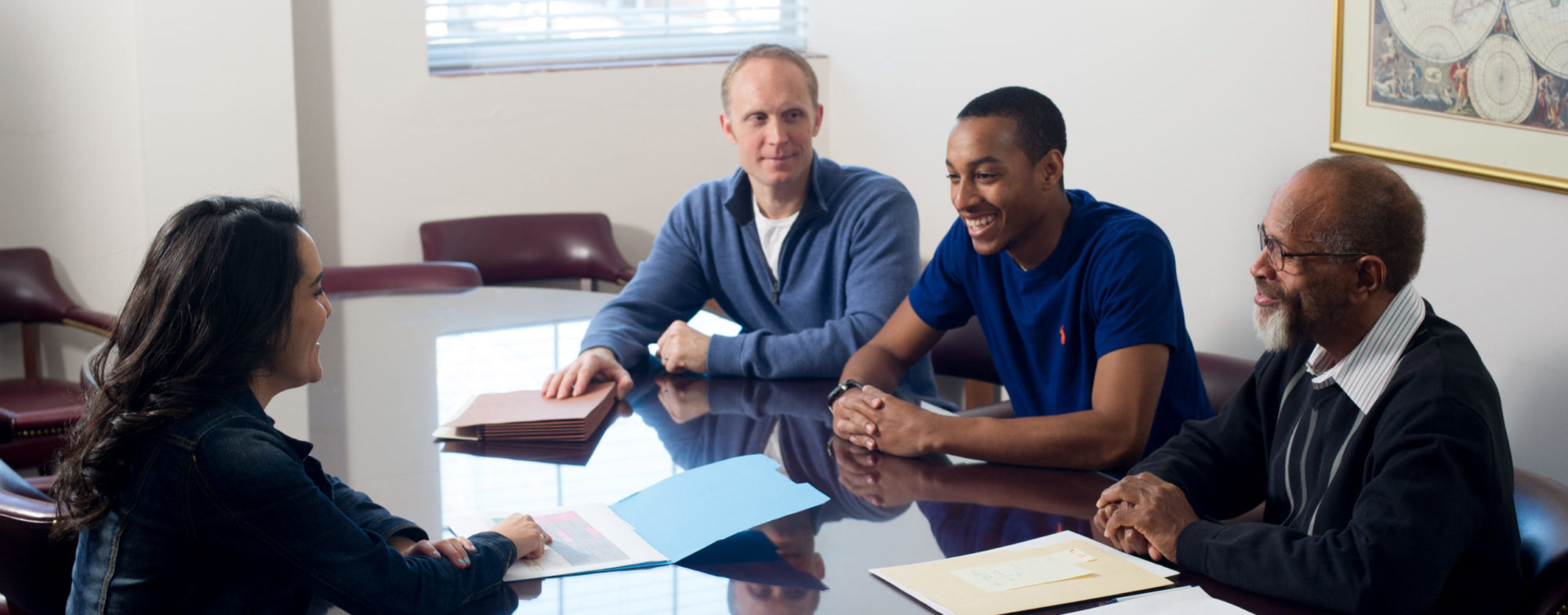 woman with three men discussing files around conference table