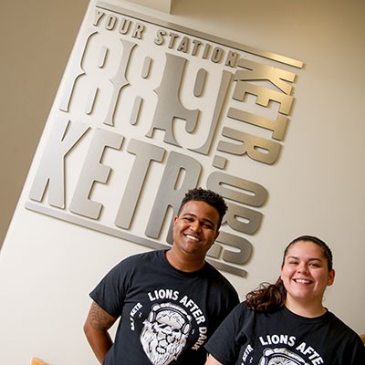 Two students taking a picture infront of the 88.9 KETR radio sign.