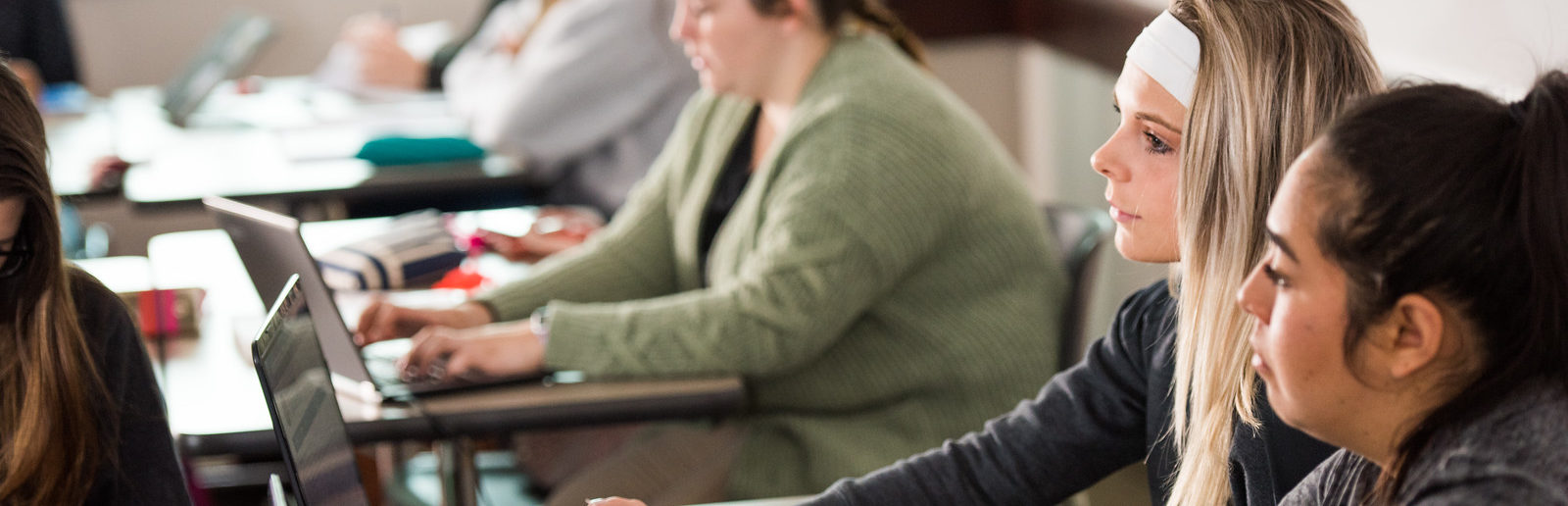 Female students in classroom listening with laptop in front of them