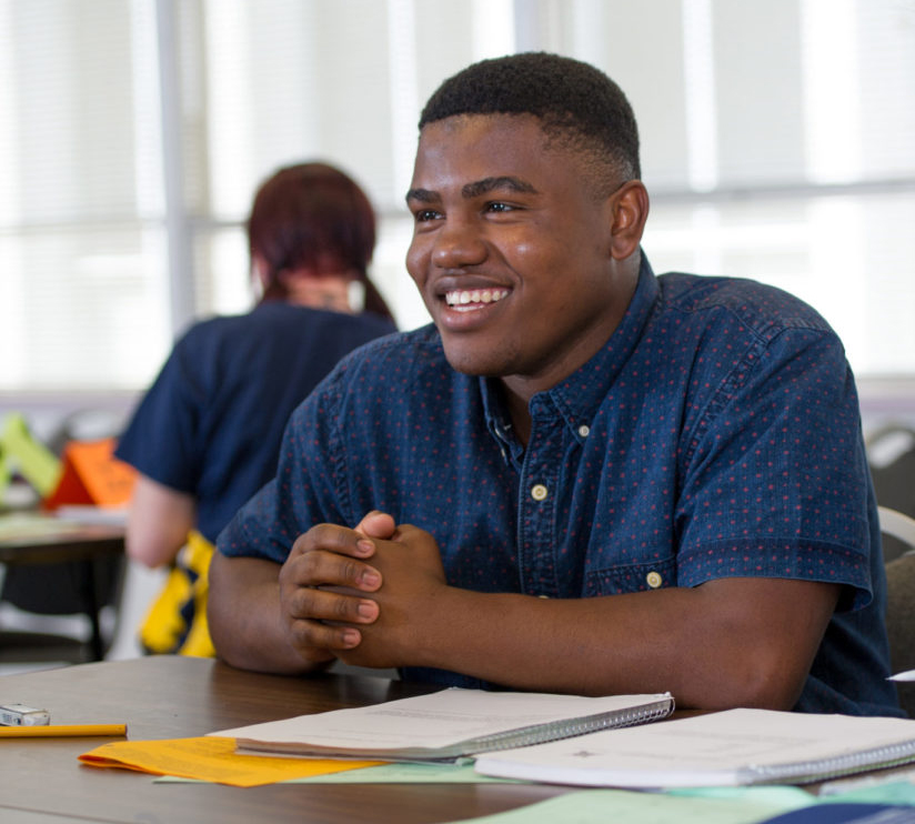 Male student sitting down in class smiling.