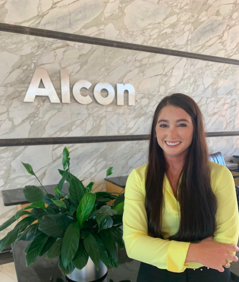 Photo of Alumni Hailey Bruening in front of Alcon sign.