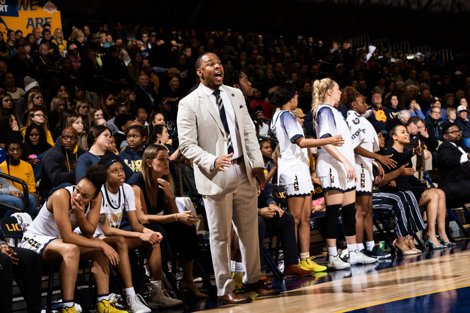 Women's basketball coach standing in front of bench coaching during game.