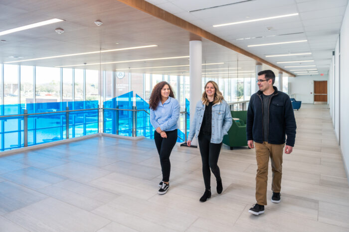 Three students walking in atrium space on second floor.