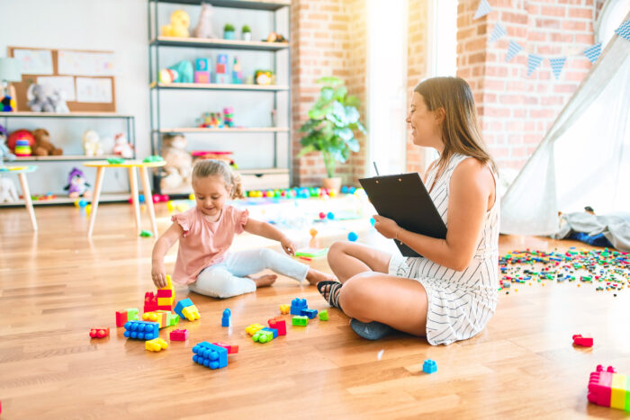 Psychologist and blond toddler girl doing therapy building tower using plastic blocks.