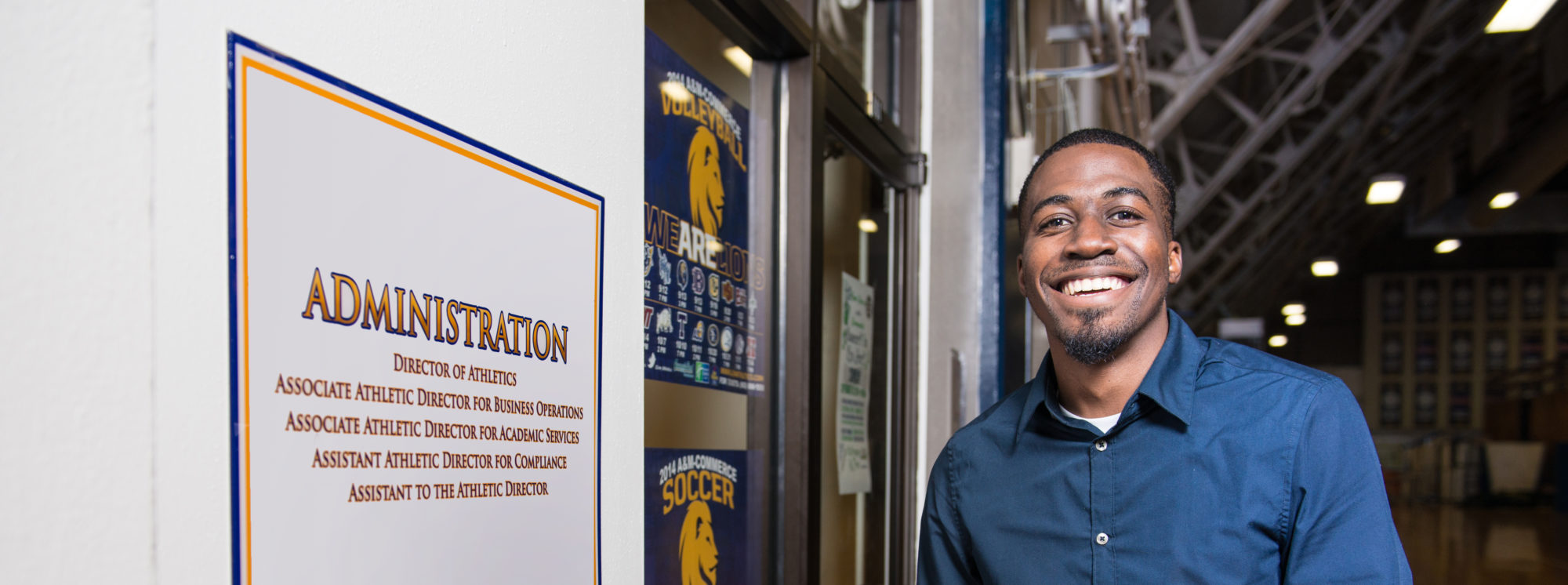 Athletic Administration Student smiling at the camera by the door of the TAMUC Athletics administration department. 