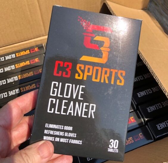 The black box features the C3 Sports logo with text indicating it eliminates odor, refreshes gloves, and works on most fabrics. Other boxes of glove cleaner are visible in an open cardboard box in the background.