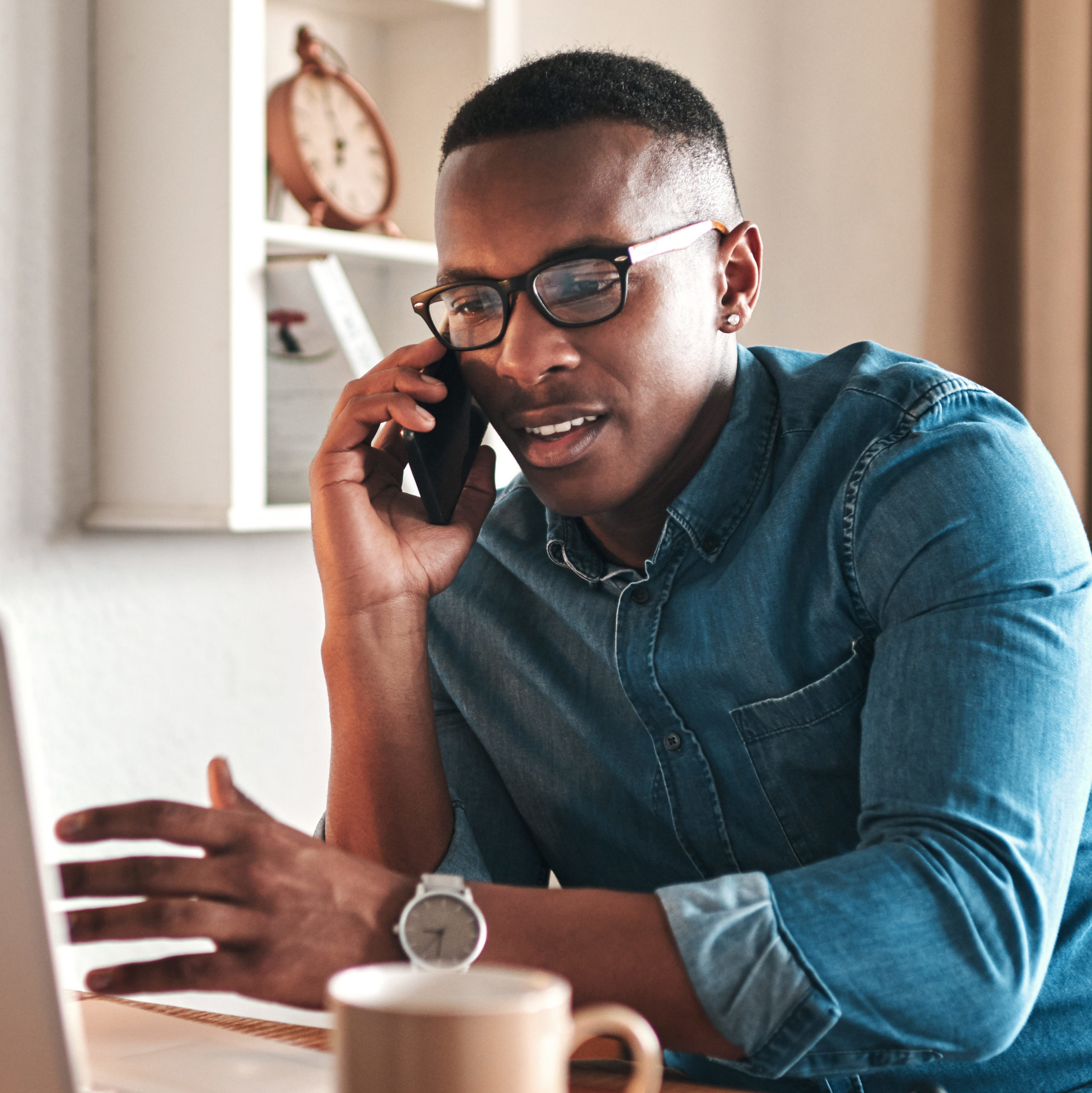 Young businessman sitting down in front of a computer talking on the cellphone.