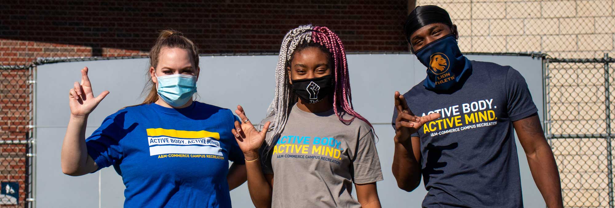 Three A&M-Commerce students wearing mask making the lion sign.
