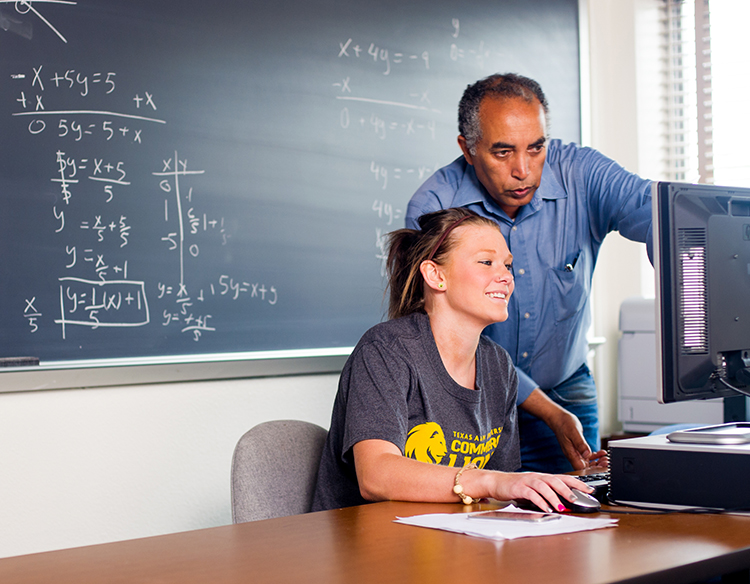 Professor helping young student sitting in front of a computer.