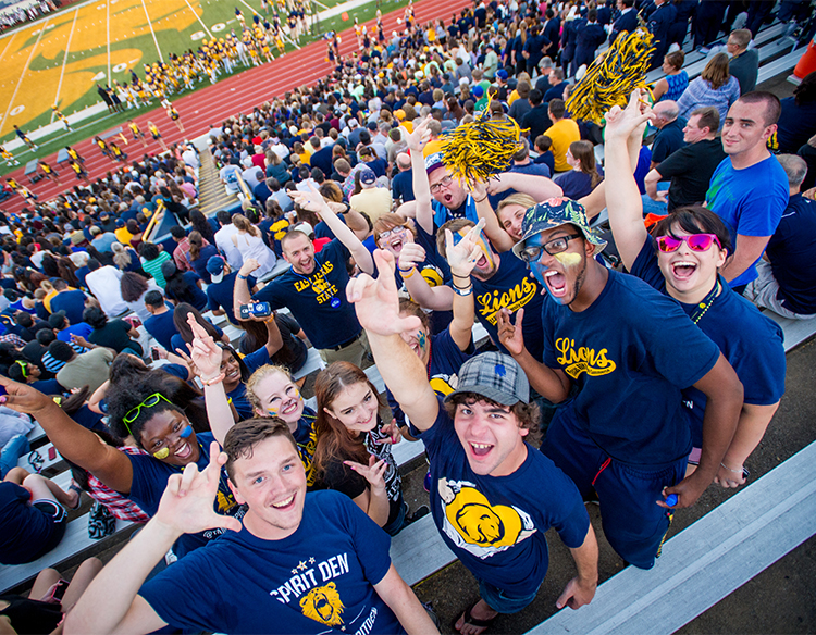 Students smiling at the camera in the student section at football game. 