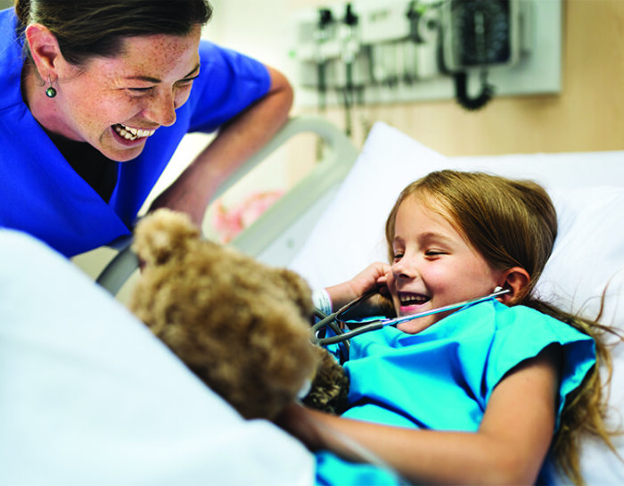 Nurse laughing with a young patient laying down in a hospital bed.