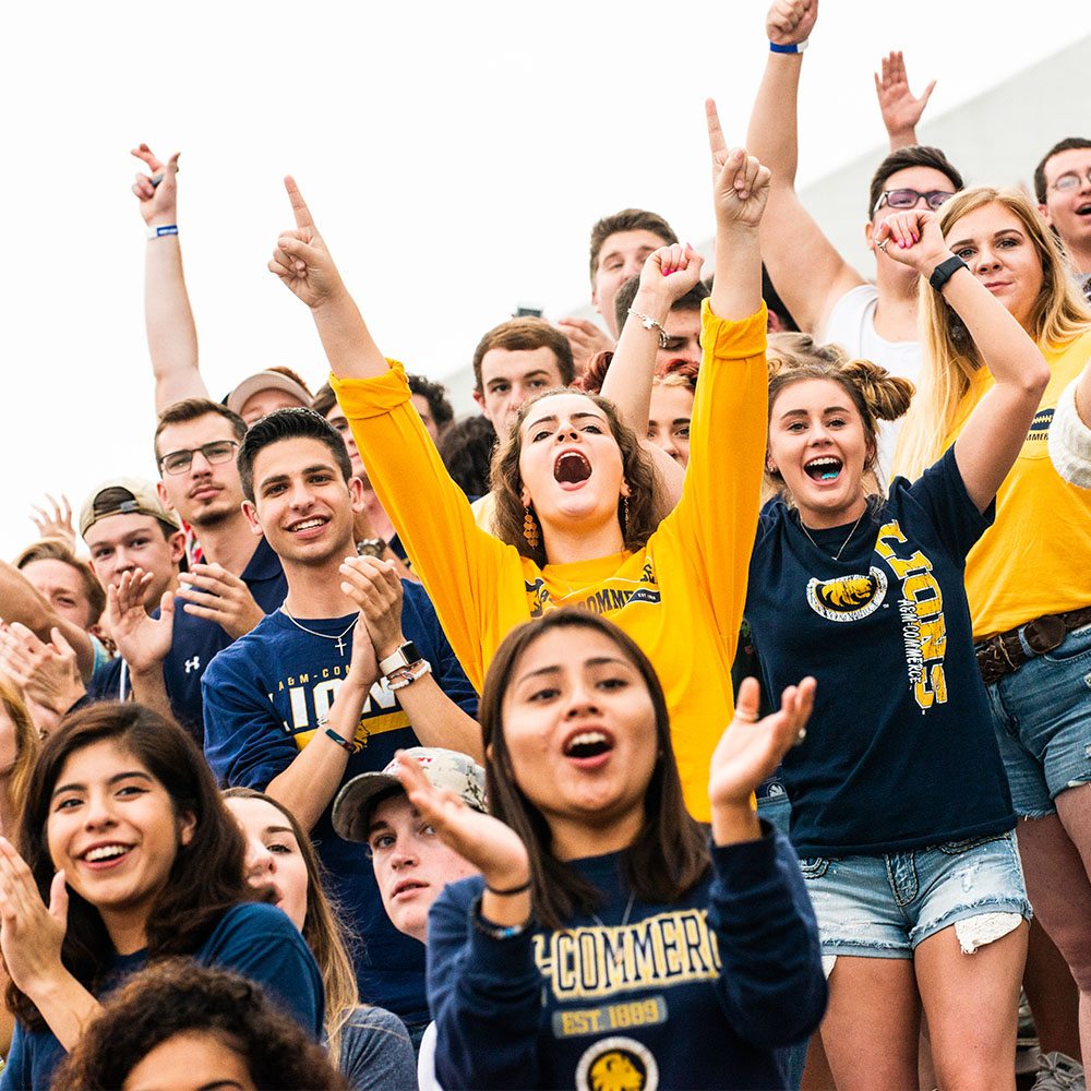 Student section at football game cheering and wearing blue shirts and gold shirts.