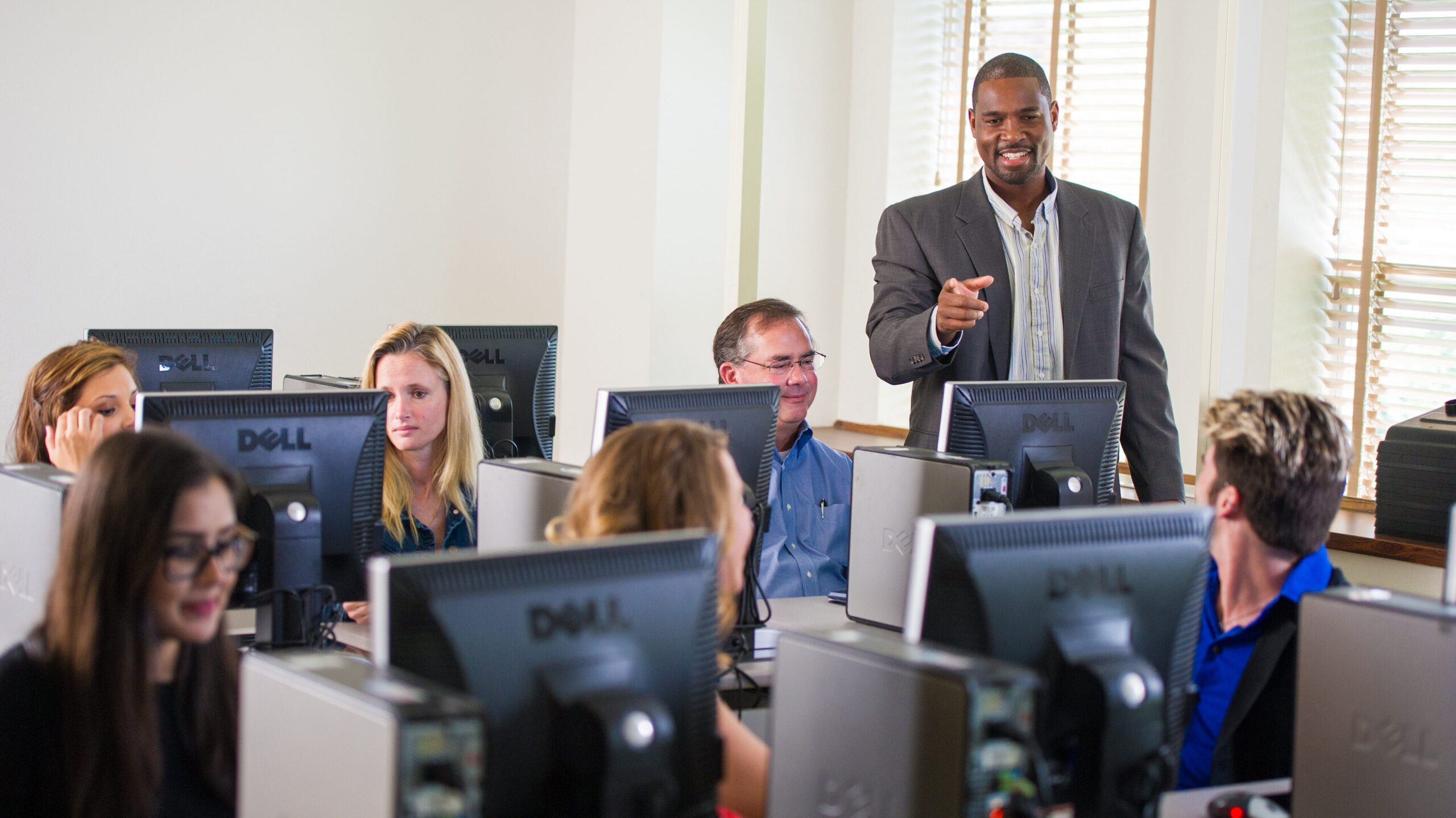 Professor in the computer lab with students sitting down in front of the screens.