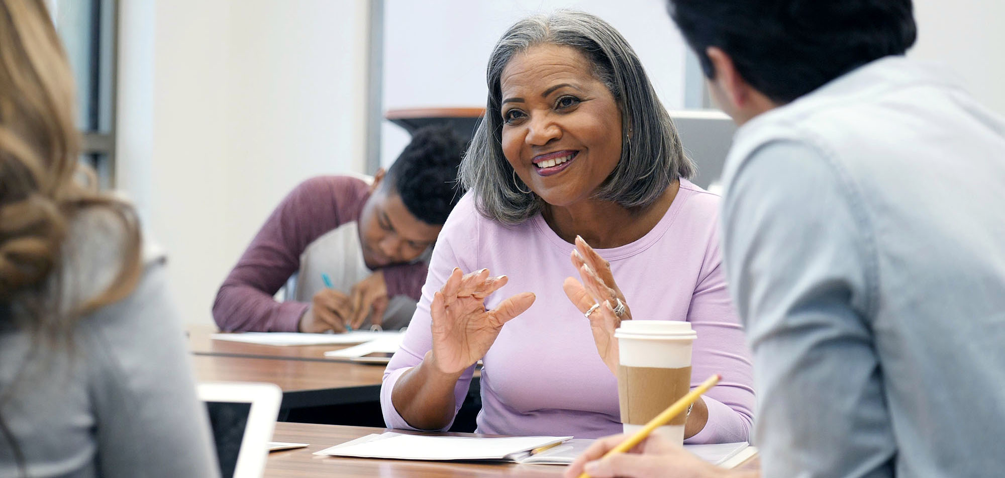 Beautiful mature African American female college student gestures as she discusses something during a study group session with classmates.